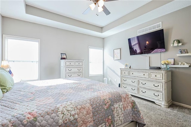 carpeted bedroom with ceiling fan and a raised ceiling