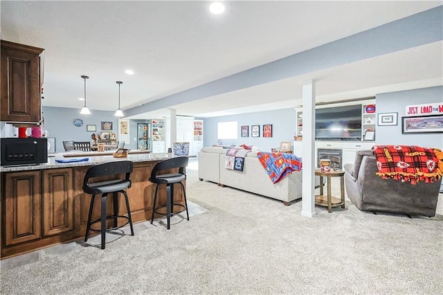 kitchen featuring pendant lighting, a kitchen bar, dark brown cabinetry, light stone countertops, and light carpet