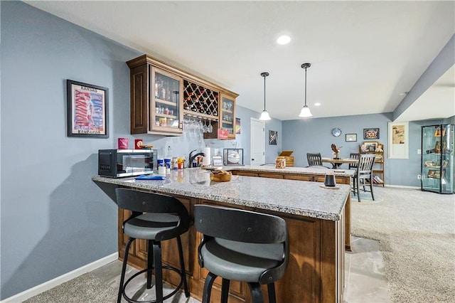 kitchen with decorative light fixtures, a kitchen breakfast bar, light colored carpet, kitchen peninsula, and light stone countertops