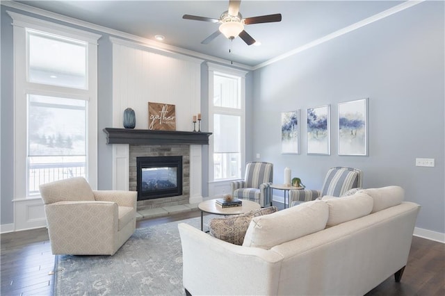 living area featuring wood finished floors, a ceiling fan, baseboards, ornamental molding, and a glass covered fireplace