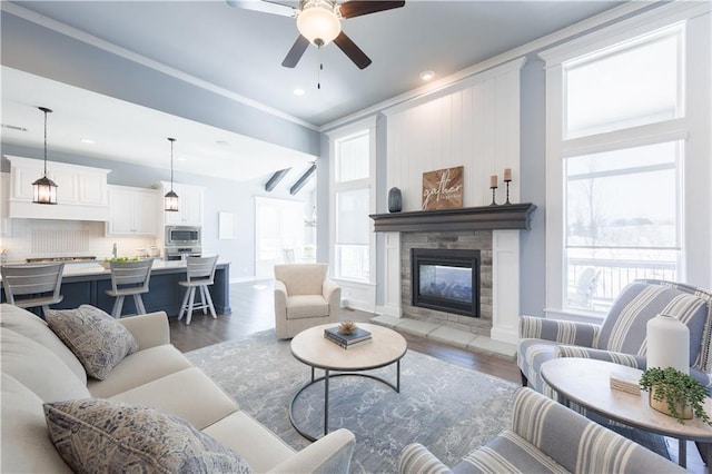 living room featuring ceiling fan, a fireplace, baseboards, and wood finished floors