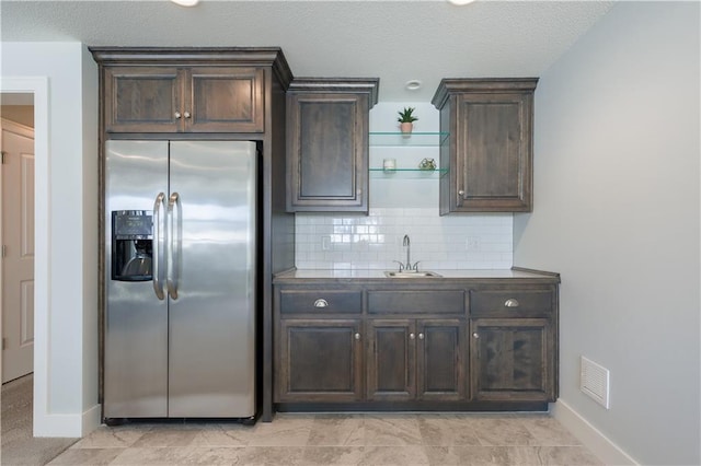 kitchen featuring dark brown cabinetry, tasteful backsplash, visible vents, stainless steel refrigerator with ice dispenser, and a sink