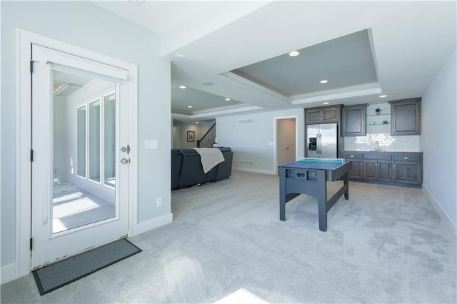 rec room featuring a tray ceiling, recessed lighting, light colored carpet, a sink, and baseboards