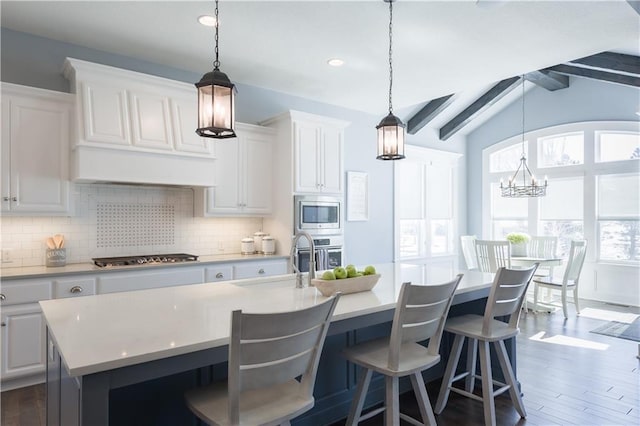 kitchen with a sink, light countertops, appliances with stainless steel finishes, decorative backsplash, and a center island with sink