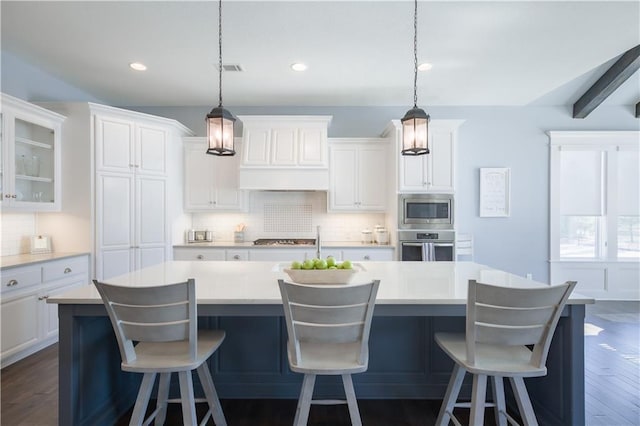 kitchen with stainless steel appliances, tasteful backsplash, custom range hood, white cabinets, and a large island with sink