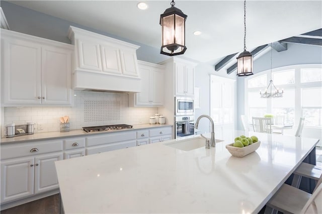 kitchen with a sink, appliances with stainless steel finishes, custom exhaust hood, backsplash, and an island with sink