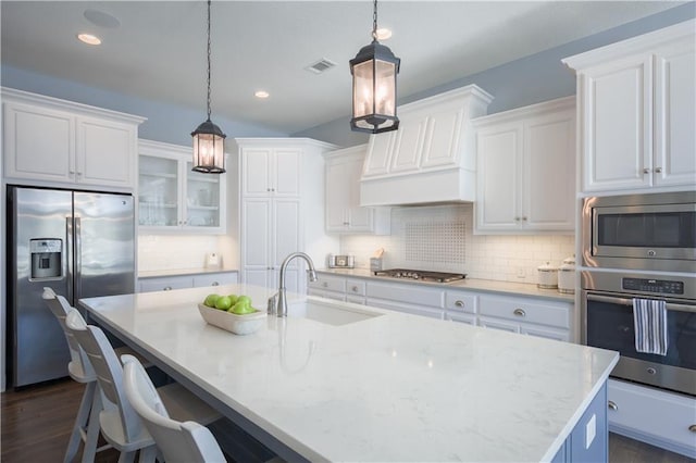 kitchen with visible vents, custom range hood, appliances with stainless steel finishes, a kitchen island with sink, and a sink