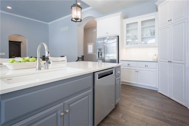 kitchen featuring arched walkways, a sink, appliances with stainless steel finishes, dark wood finished floors, and crown molding