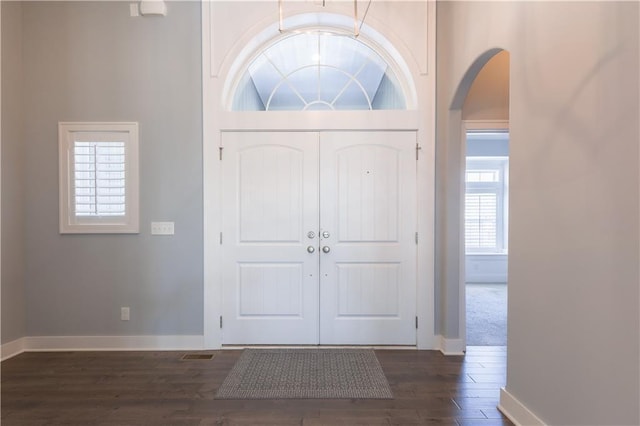 entrance foyer with arched walkways, visible vents, dark wood finished floors, and baseboards