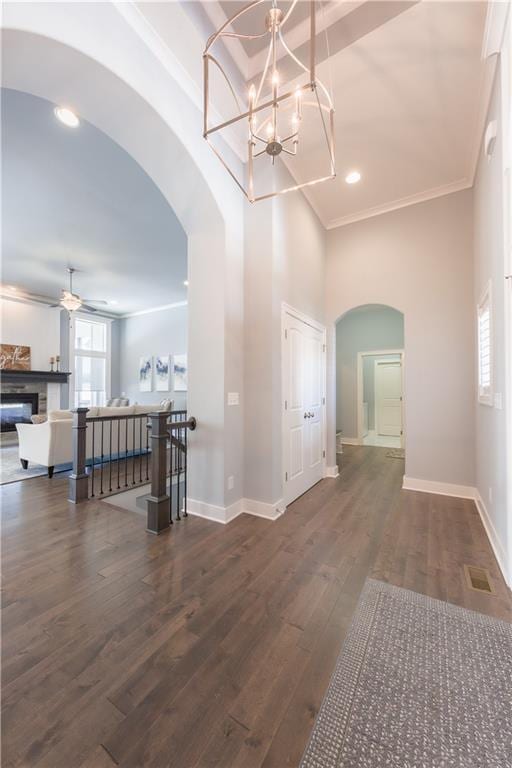 interior space featuring baseboards, arched walkways, visible vents, wood finished floors, and crown molding