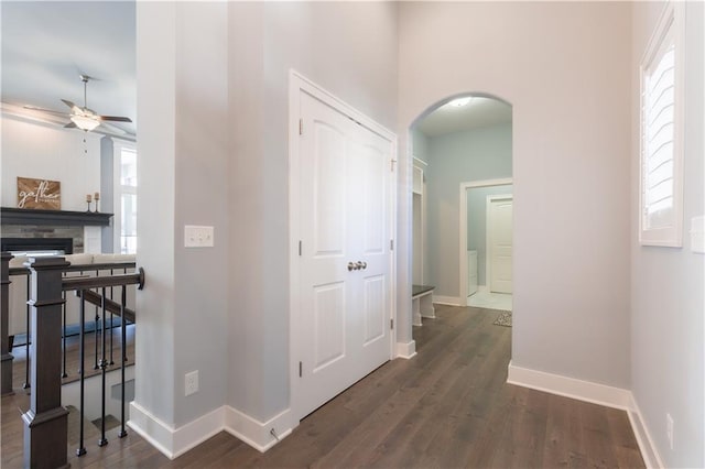 corridor featuring baseboards, arched walkways, and dark wood-type flooring