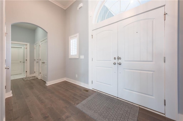 foyer featuring dark wood-style floors, arched walkways, ornamental molding, and baseboards