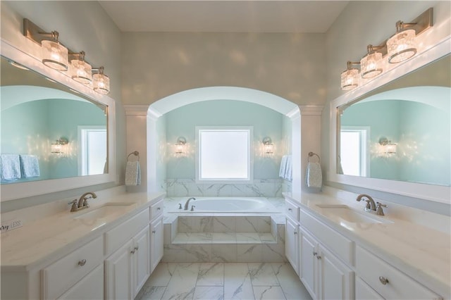 full bath with a garden tub, marble finish floor, two vanities, and a sink