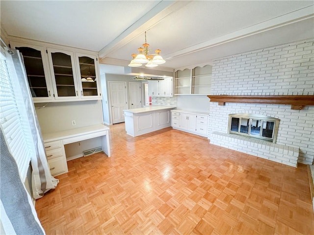 kitchen featuring built in desk, white cabinets, hanging light fixtures, light parquet flooring, and a brick fireplace