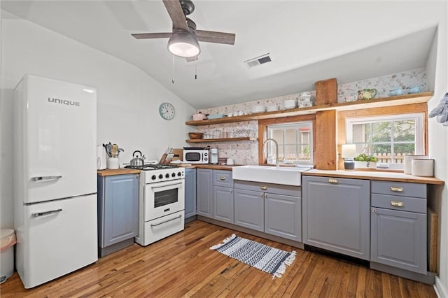 kitchen featuring lofted ceiling, sink, gray cabinetry, white appliances, and light hardwood / wood-style floors