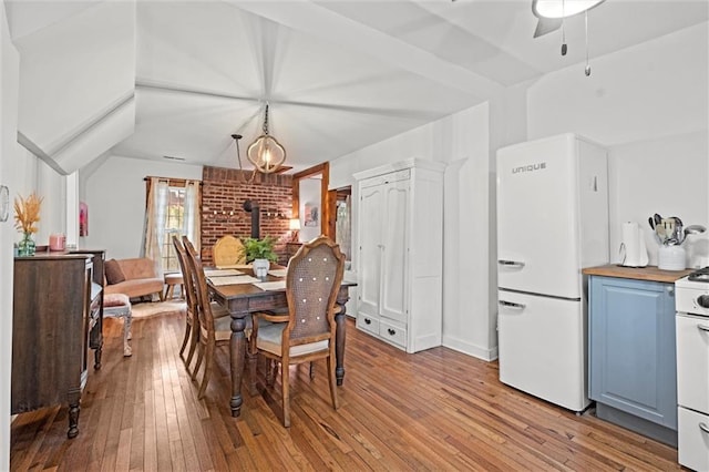 dining room featuring vaulted ceiling, light hardwood / wood-style floors, and a wood stove