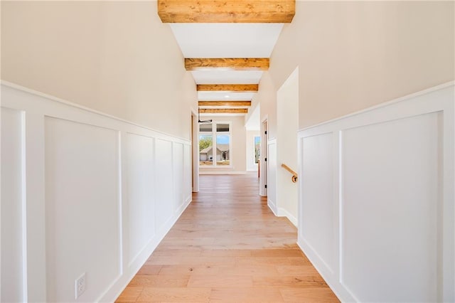 corridor with a decorative wall, light wood-style floors, beam ceiling, and wainscoting