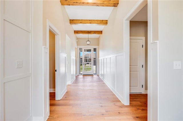 hallway with beamed ceiling, baseboards, and light wood-type flooring