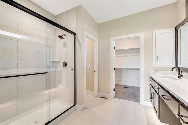 bathroom with a shower stall, baseboards, a walk in closet, and vanity