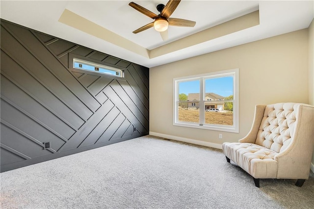 living area with baseboards, a ceiling fan, a tray ceiling, and carpet