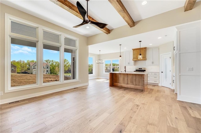 unfurnished living room with a sink, ceiling fan with notable chandelier, beamed ceiling, light wood finished floors, and recessed lighting