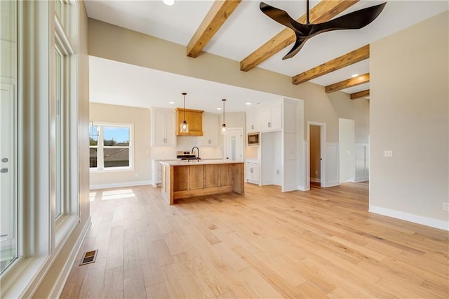 kitchen with light wood-style flooring, beam ceiling, a sink, visible vents, and light countertops