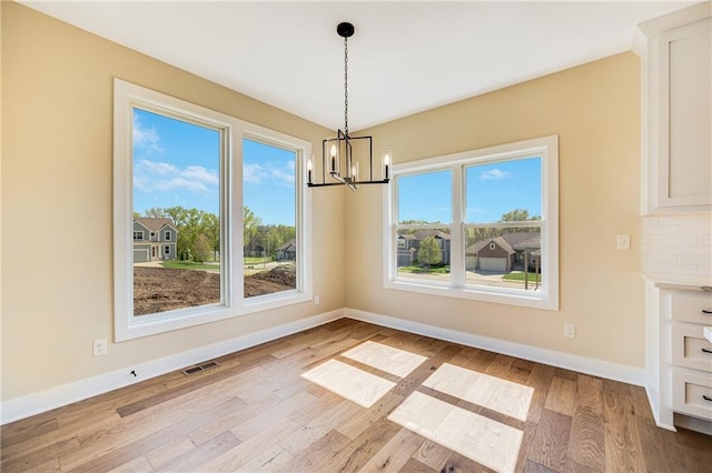 unfurnished dining area with baseboards, wood finished floors, a chandelier, and visible vents