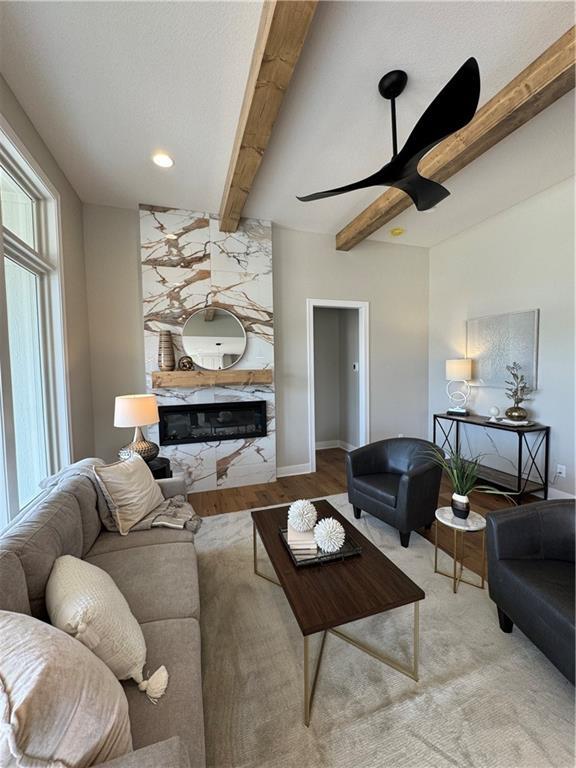 living room with ceiling fan, wood finished floors, beam ceiling, and a high end fireplace