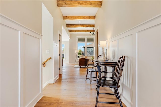 corridor featuring baseboards, light wood-style floors, and beamed ceiling