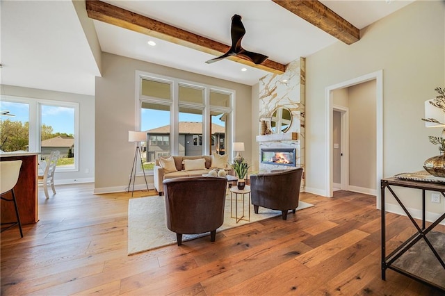 living area featuring recessed lighting, light wood finished floors, beamed ceiling, baseboards, and a large fireplace