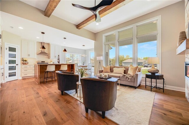 living room featuring recessed lighting, a ceiling fan, beamed ceiling, baseboards, and light wood-style flooring