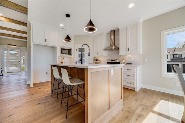 kitchen featuring wall chimney range hood, decorative backsplash, white cabinetry, and light countertops