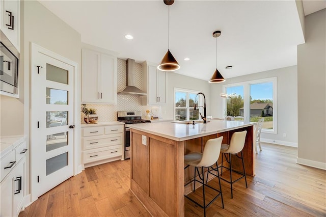 kitchen with light wood-style flooring, a sink, wall chimney range hood, light countertops, and appliances with stainless steel finishes