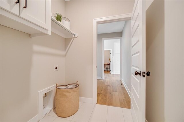 washroom with electric dryer hookup, baseboards, and cabinet space
