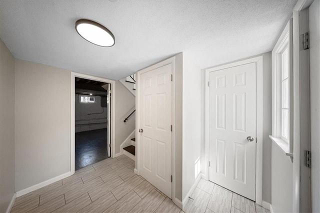 hall featuring stairs, wood finish floors, baseboards, and a textured ceiling