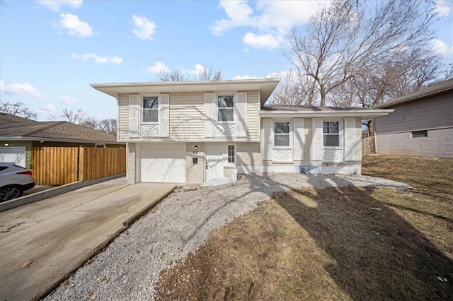 tri-level home with brick siding, an attached garage, driveway, and fence