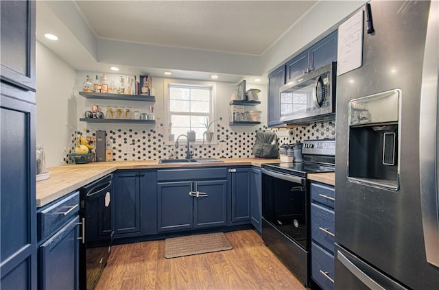 kitchen with sink, butcher block counters, black appliances, blue cabinets, and light wood-type flooring