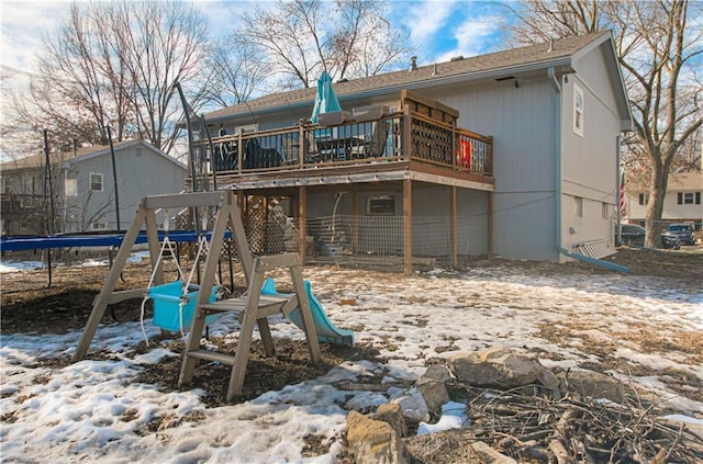 snow covered house with a trampoline, a playground, and a deck