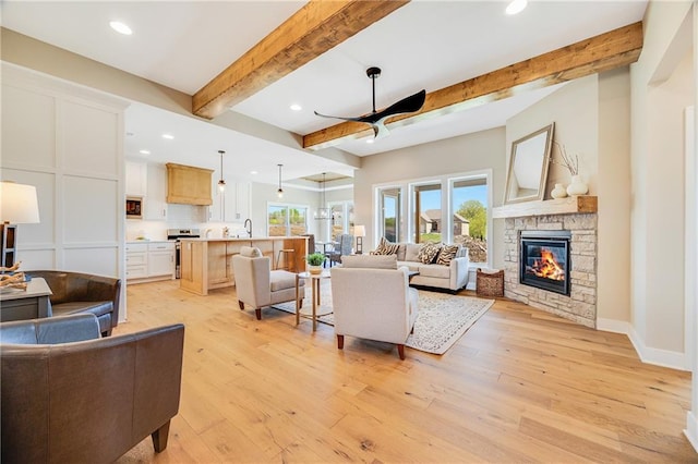 living room featuring recessed lighting, a ceiling fan, beamed ceiling, light wood-style floors, and a fireplace