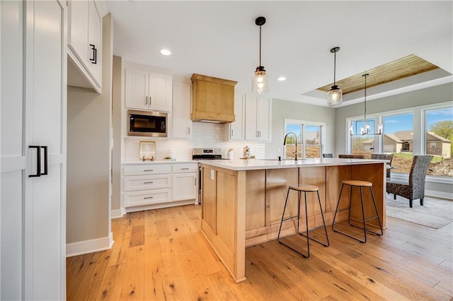 kitchen with built in microwave, decorative backsplash, stainless steel gas stove, a tray ceiling, and light wood-style flooring