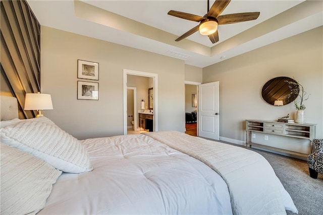 carpeted bedroom featuring a tray ceiling, visible vents, baseboards, ceiling fan, and ensuite bath