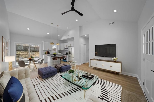 living area featuring visible vents, baseboards, recessed lighting, light wood-style flooring, and high vaulted ceiling