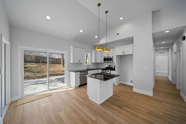 kitchen featuring wood finished floors, a sink, appliances with stainless steel finishes, white cabinetry, and dark countertops