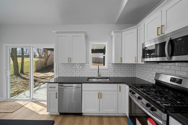 kitchen featuring dark countertops, backsplash, light wood-type flooring, stainless steel appliances, and a sink