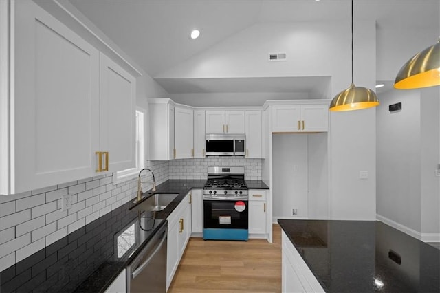 kitchen with dark stone countertops, white cabinets, stainless steel appliances, and a sink