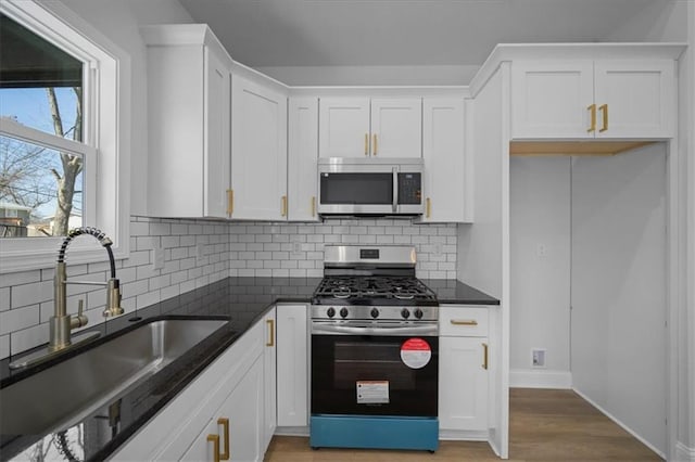 kitchen featuring backsplash, light wood-style flooring, white cabinets, stainless steel appliances, and a sink