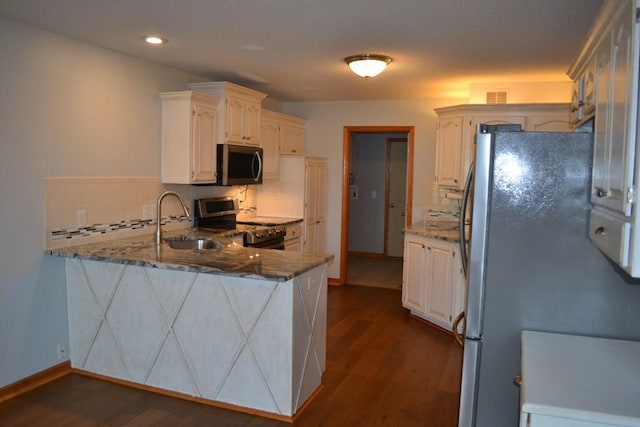 kitchen with appliances with stainless steel finishes, white cabinetry, sink, dark stone counters, and kitchen peninsula