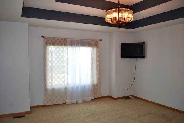 unfurnished room featuring a raised ceiling, carpet, and a chandelier