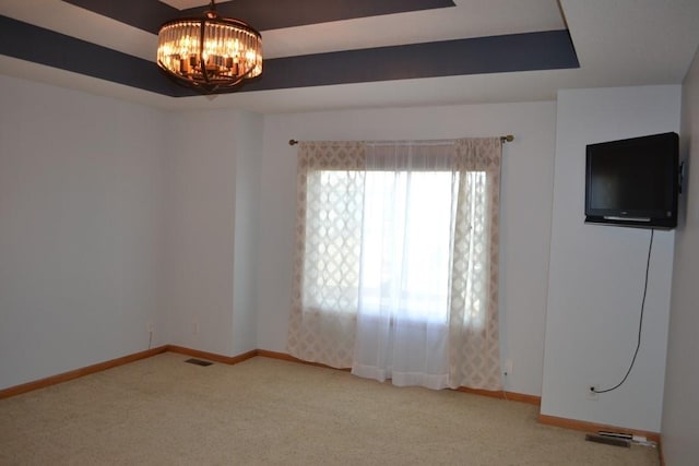 carpeted empty room featuring a tray ceiling and a chandelier