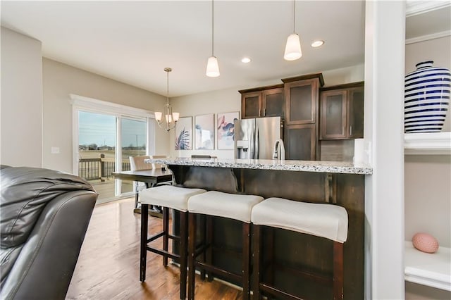 kitchen with stainless steel fridge with ice dispenser, dark brown cabinets, light stone countertops, and hanging light fixtures